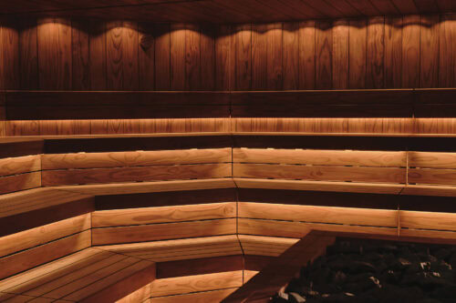 Contemporary sauna interior with Thermory thermo-radiata pine walls and dark thermo-alder details, illuminated by soft indirect lighting.