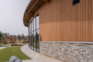 Lähivaade Clopton Farms kogukonnakeskuse kaarduvast fassaadist Thermory Benchmark termotöödeldud radiata männi voodriga ja kivist alusdetailiga.