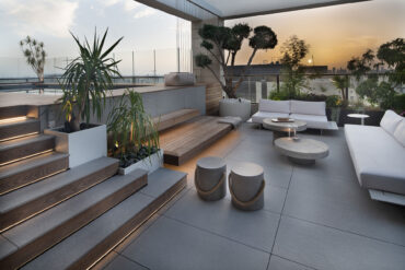 Penthouse-terassi Thermoryn lämpökäsitellyillä saarniterassilaudoilla ja sisäänrakennetuilla istuimilla, näkymä kaupungin ylle auringonlaskussa.