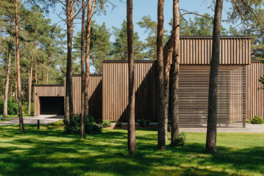 Moderni talo mäntyjen keskellä Thermoryn lämpösaarni-verhouksella ja terassilla, joka sulautuu luontoon.