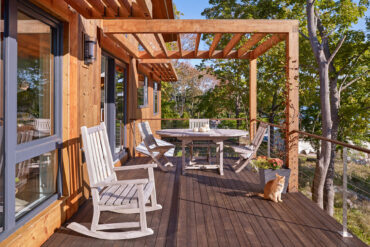 Außenterrasse mit Pergola und Thermory Benchmark Thermo-Esche Decking, umgeben von Bäumen und Tageslicht.