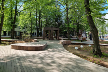 Kaarevat Thermoryn lämpösaarnikävelytiet ja istuma-alueet kulkevat varjoisan puistoalueen halki.