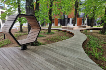 Hexagonale Sitzstruktur und Gehweg aus Thermory Thermo-Esche, die sich harmonisch in die Waldlandschaft einfügen.