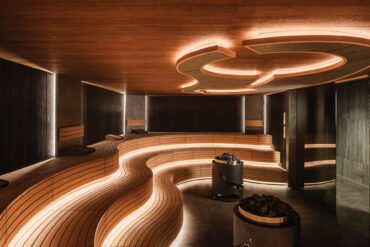 Sauna Événementiel at Les Bains de Lavey with flowing bench geometry, Thermory Sauna Ignite wall panels, and glowing alder seating elements.