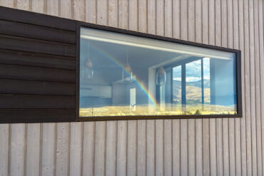 Passive house exterior with Thermory Vivid Silvered and Vivid Opaque Black cladding reflecting mountain scenery through large window.