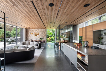 Open-plan living and kitchen area with Thermory thermo-radiata pine ceiling and stone wall accents.