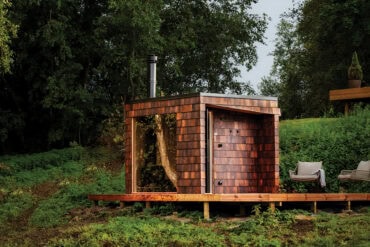 Jõeäärne saun, mille fassaad on kaetud Thermory termosaare sindlitega looduslikes pruunides toonides, sulandudes harmooniliselt metsa ja vee keskele.