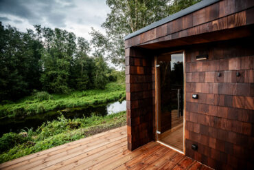 Lähivaade River Side Sauna termosaare sindlitel ja puidust terrassil, kust avaneb rahulik vaade jõele ja rohelisele maastikule.