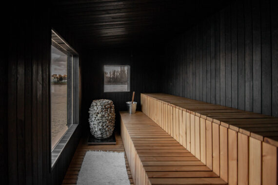 Interior of Sauna Bobor with black-painted Thermory alder walls and warm wooden benches overlooking the Danube through large windows.