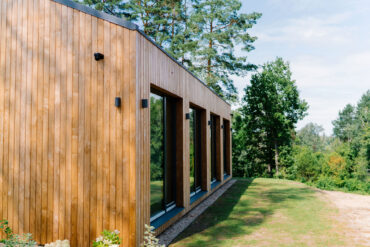 Lähivaade Thermory termoradiata männi voodrist suurte akende ja metsataustaga.