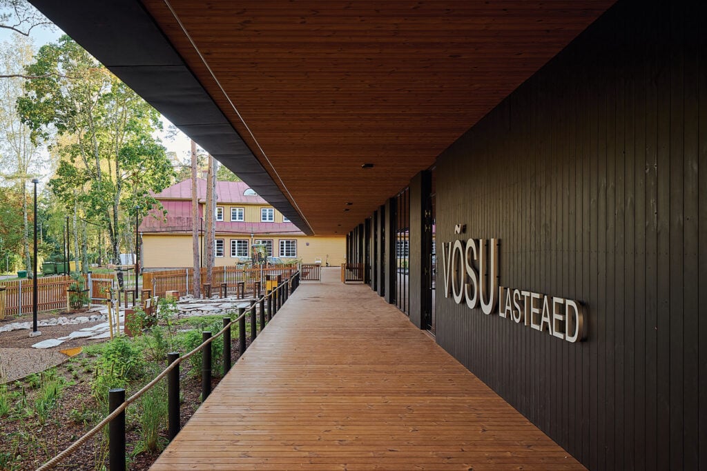Covered wooden walkway at Võsu Kindergarten featuring oiled Thermory thermo-pine decking and dark façade cladding.