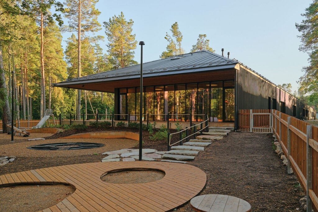Daytime view of Võsu Kindergarten playground surrounded by pine forest and Thermory thermo-pine façade.